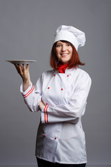 Photo of smiling chef girl in white coat with an empty plate