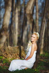 beautiful woman in white dress sits by tree green forest.
