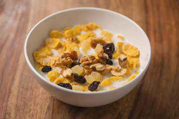 corn flakes with nuts and fruits in white bowl on wood table