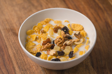 corn flakes with nuts and fruits in white bowl on wood table