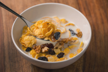 corn flakes with nuts and fruits in white bowl on wood table