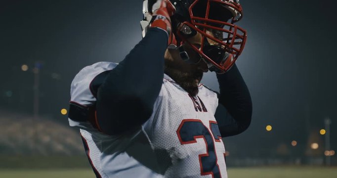 American football player putting on his protective helmet against bright stadium illumination lights