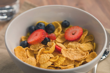 corn flakes with berries in white bowl for breakfast on table