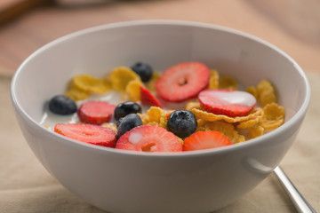 corn flakes with berries in white bowl for breakfast on table
