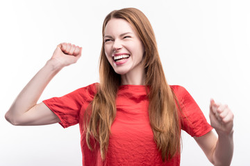 Emotional reaction. Upbeat ginger-haired young woman raising her hands in a gesture of celebration and laughing happily, having heard good news