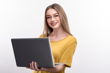 Fototapeta premium Young professional. Cheerful pretty woman in a mustard blouse holding a laptop and posing with it, isolated on a white background, while wearing eyeglasses