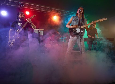 Rock band performs on stage. Guitarist, bass guitar and drums.