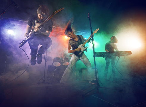Rock band performs on stage. Guitarist, bass guitar and drums. Stock Photo  | Adobe Stock