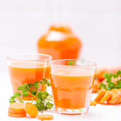 Carrot juice in beautiful glasses, cut orange vegetables and green parsley on white wooden background. Fresh orange drink. Close up photography. Selective focus. Horizontal banner