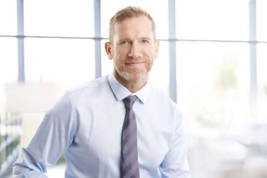 Executive businessman at the office. Smiling senior investment advisor business man wearing shirt and tie while standing at the office and looking at camera.