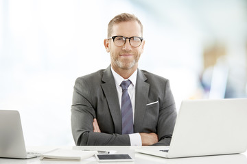 Middle aged businessman with laptop. Portrait of mature senior male agent wearing shirt and tie while sitting at desk and working on laptop at the office. 