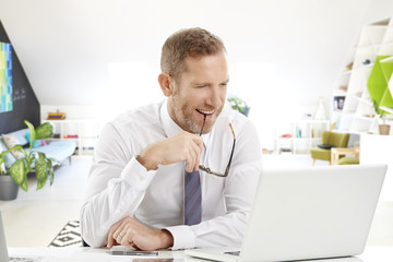 Middle aged businessman with laptop. Portrait of mature senior male agent wearing shirt and tie while sitting at desk and working on laptop at the office. 