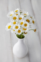 Chamomiles or daisies in white vase on wooden planks, summer flowers composition