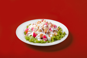 Salad with crab meat, breadcrumbs on a monophonic red background. It is decorated with lettuce leaves. Side view