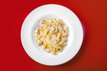 Pasta, noodles with chicken, turkey, decorated with cheese. Monochrome red background. Dish for the menu of the restaurant, bar, cafe. View from above