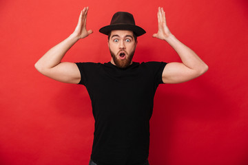 Photo of joyous attractive man with beard in casual emotionally throwing hands up on in air, isolated over red background