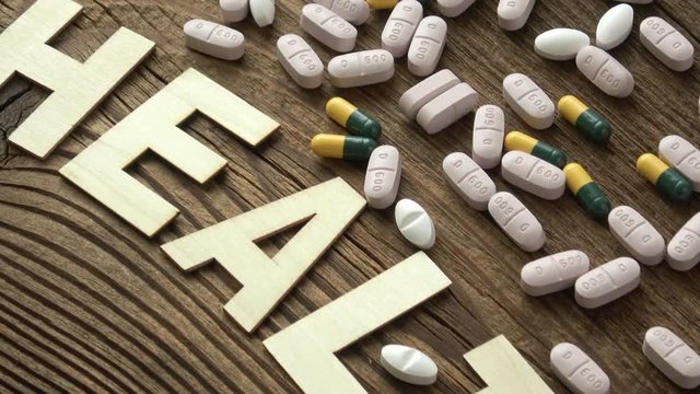 Pills with inscription HEALTH on brown wooden surface background