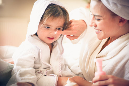 Mother and daughter after bath play with body lotion.