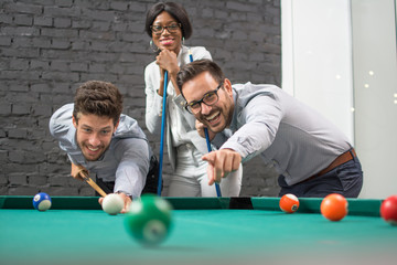 Cheerful  business colleagues playing billiards after work.