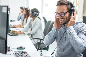 Smiling customer service executive with headset working in call center. - obrazy, fototapety, plakaty