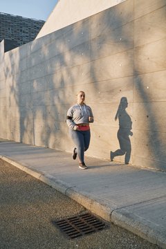 Curvaceous young female runner running along sidewalk