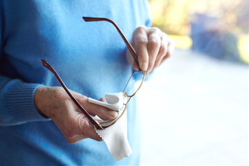 Senior woman cleaning eyeglasses with cloth, mid section