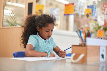Schoolgirl writing at classroom desk in primary school