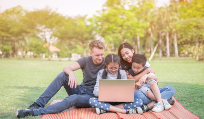 Fototapeta na wymiar Modern family using laptop while resting in park