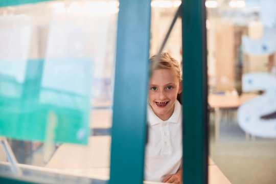 Portrait of schoolgirl looking through classroom window at primary school