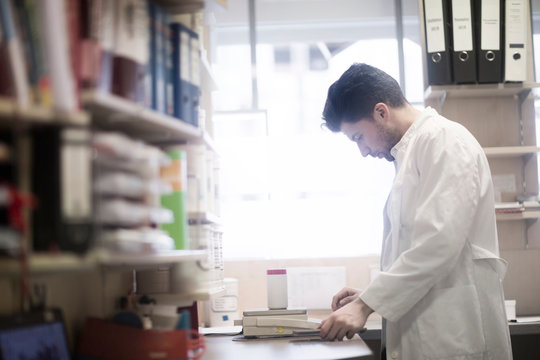 Young male pharmacist weighing pill bottle on pharmacy scales