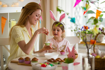 Mother and daughter celebrating Easter, cooking cupcakes, covering with glaze. Happy family...