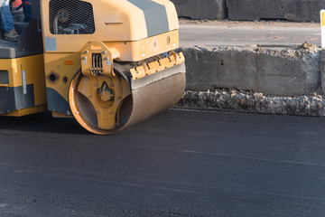 Side view small yellow ride on roller asphalt compactor aligns the road. Laying new asphalt....