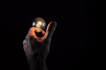 Male hand with incandescent light bulb on black background.
