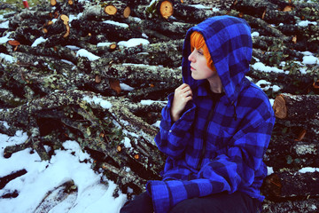 Adolescente en la nieve en un día de invierno sobre unos troncos de leña 