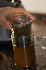 Fototapeta na wymiar Making tea (green tea leaves) in a glass cup, wit two pieces, green tea leaves with hot water in a transparent clear cup with a kettle near it, making tea with kettle