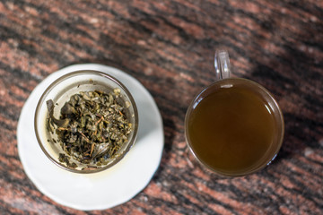 Making tea (green tea leaves) in a glass cup, wit two pieces, green tea leaves with hot water in a transparent clear cup with a kettle near it, making tea with kettle