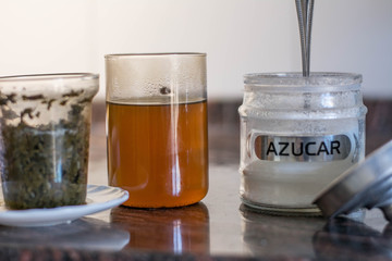 Making tea (green tea leaves) in a glass cup, wit two pieces, green tea leaves with hot water in a transparent clear cup with a kettle near it, making tea with kettle