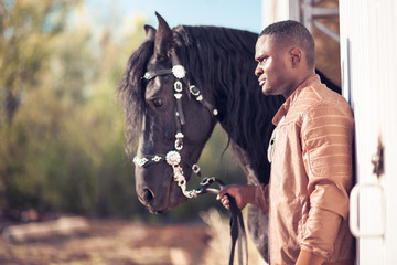 african Man wearing sunglasses near a black horse in hangar