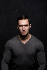 Handsome tough guy on a black background. Portrait. Brawn. Gray sweater. Force. Masculinity.