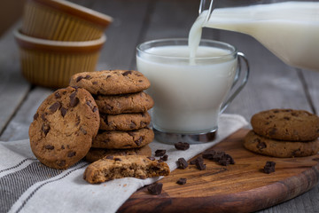Chocolate chip cookies with milk on old rustic wooden table. Milk pouring.