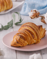 Delicious continental breakfast with fresh flaky french croissants, close up on the croissants. With white cotton flowers on a light wooden background. Provence rustic style
