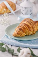 Delicious continental breakfast with fresh flaky french croissants, close up on the croissants. With white cotton flowers on a light wooden background. Provence rustic style