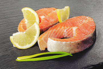 Slice of red raw fish salmon with lemon and rosemary isolated on black slate board. Food background