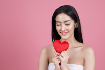 Portrait of Beautiful Asian Woman holding red heart symbol. Beautiful Woman looking to camera.  People with Youth and Skin Care Concept. isolated on pink background.