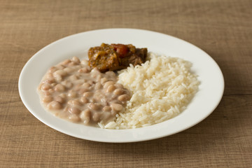 White rice, pinto beans and meat with sauce. White dish on wooden table. Detail of food dish, closeup, selective focus.