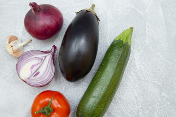 Set of raw ingredients for Italian cooking on stone table background. Eggplant, garlic, onion, tomato, zucchini. Closeup and top view