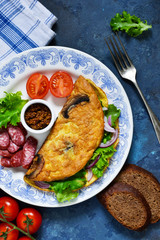 Omelette with mushrooms, cheese and spinach on a concrete blue background. Light breakfast with salami, scrambled eggs and vegetables.