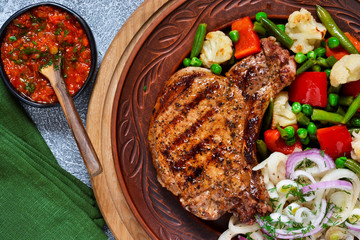 Fried steak with pickled onion and grilled vegetables on a concrete background.