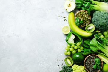 Organic green vegetables and fruits on grey background. Copy space, flat lay, top view. Green apple, zucchini, cucumber, avocado, kale, lime, kiwi, grapes, banana, broccoli, marbled lentils, mung bean