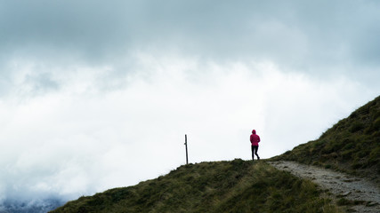 A hiker walking along a path to the top of a hill with a storm approaching in the distance